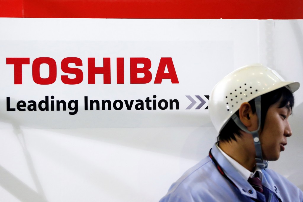 An employee stands next to a logo of Toshiba Corp during a demonstration of the company's new four-legged robot, at the company's Yokohama complex in Yokohama, south of Tokyo