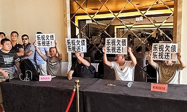 二十多名樂視移動的供應商在股東大會場內，舉起印有「樂視欠債樂視還」字句的紙牌抗議。（網上圖片）
