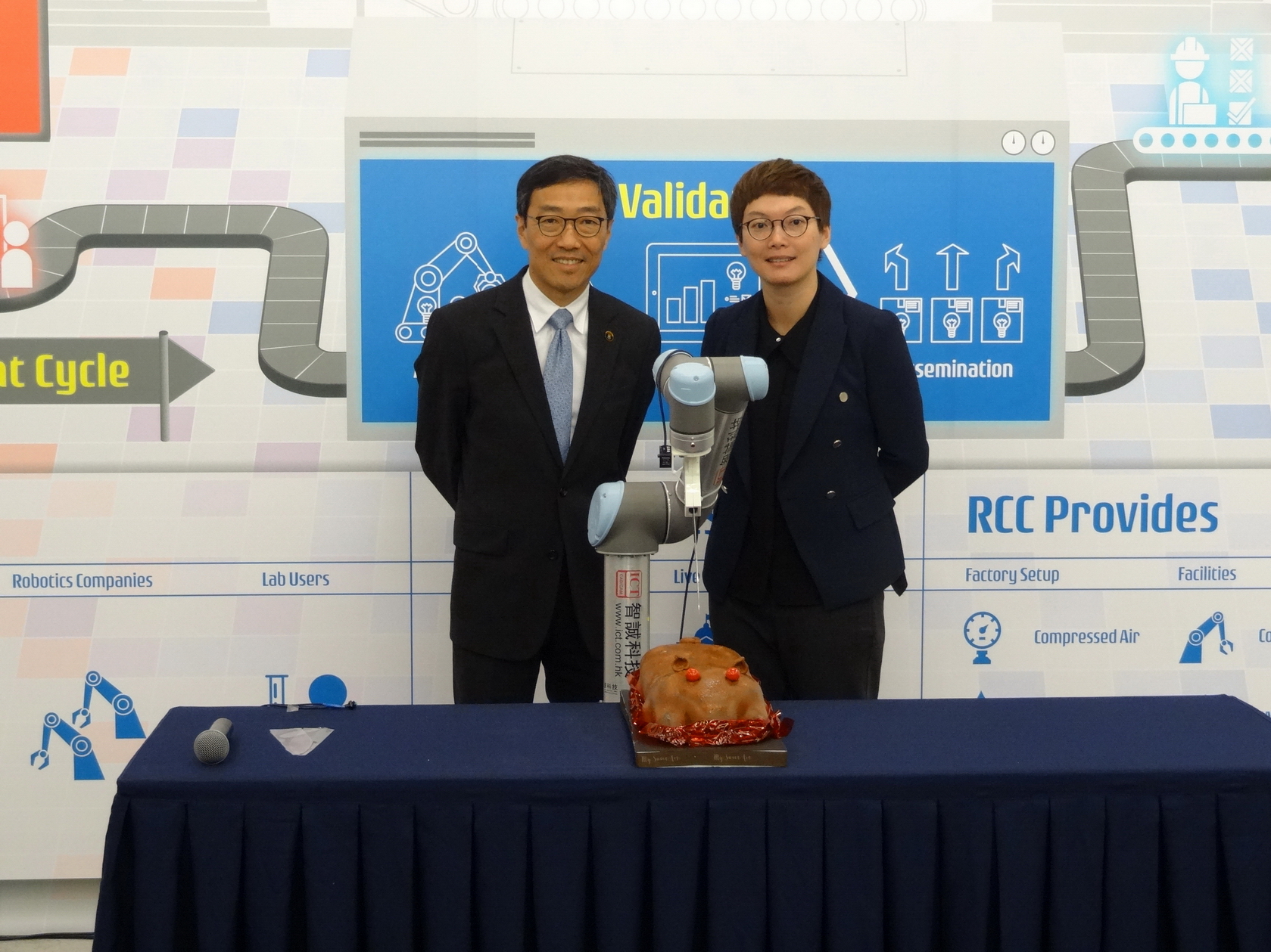 香港科技園公司行政總裁黃克強（左）及香港科技園公司技術主管（機械人技術）霍露明博士（右）以機械臂切燒豬蛋糕的儀式，慶祝機械人技術促進中心正式開幕。
