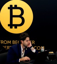 A man works on a laptop beneath the Bitcoin logo at the Consensus 2018 blockchain technology conference in New York City