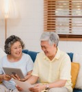 Asian elderly couple using tablet watching TV in living room at